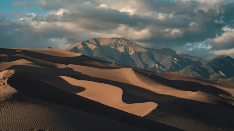 golden desert sand dunes with dramatic cloudy sky and mountain backdrop landscape wallpaper