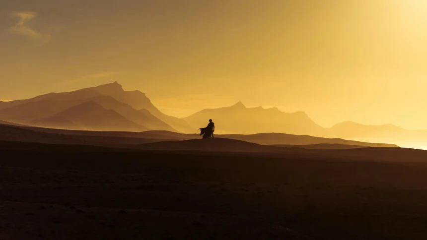 Lone figure walking across the golden Arrakis desert landscape at sunset from Dune Part Two wallpaper