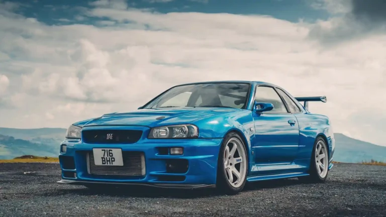 Blue Nissan Skyline GT-R R34 parked on scenic road with dramatic cloudy sky wallpaper
