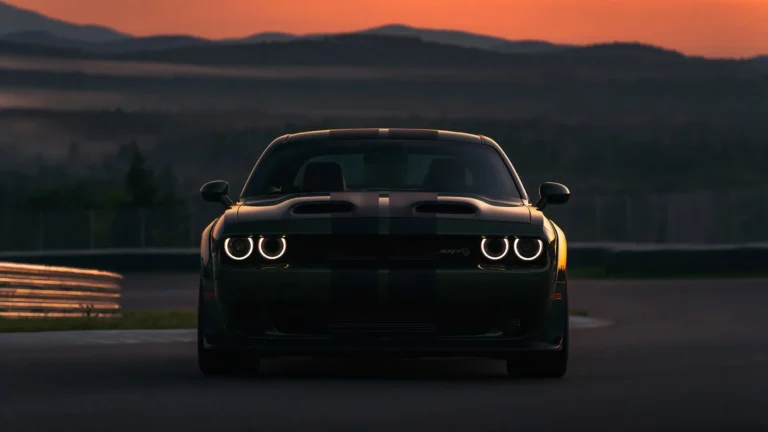 Black Dodge Challenger SRT Hellcat parked on a racetrack at sunset with glowing headlights and dramatic evening landscape wallpaper