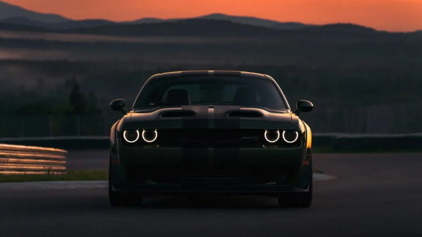 Black Dodge Challenger SRT Hellcat parked on a racetrack at sunset with glowing headlights and dramatic evening landscape wallpaper