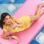 Celebrity relaxing on a pink pool float surrounded by water and ice cubes in a colorful summer fashion photoshoot wallpaper