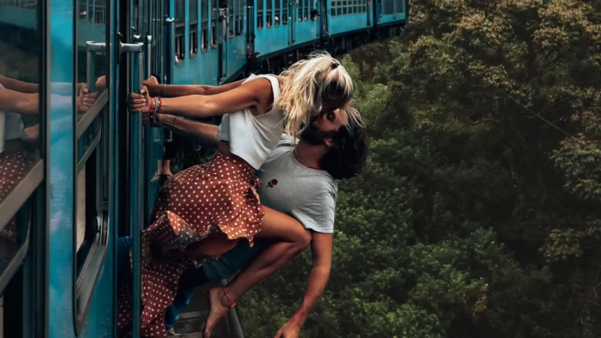 Romantic couple kissing while leaning from a moving train through a lush forest wallpaper