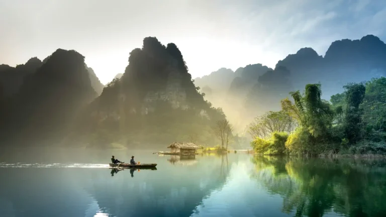 Majestic karst mountains rising above a tranquil lake with misty reflections and a small boat wallpaper