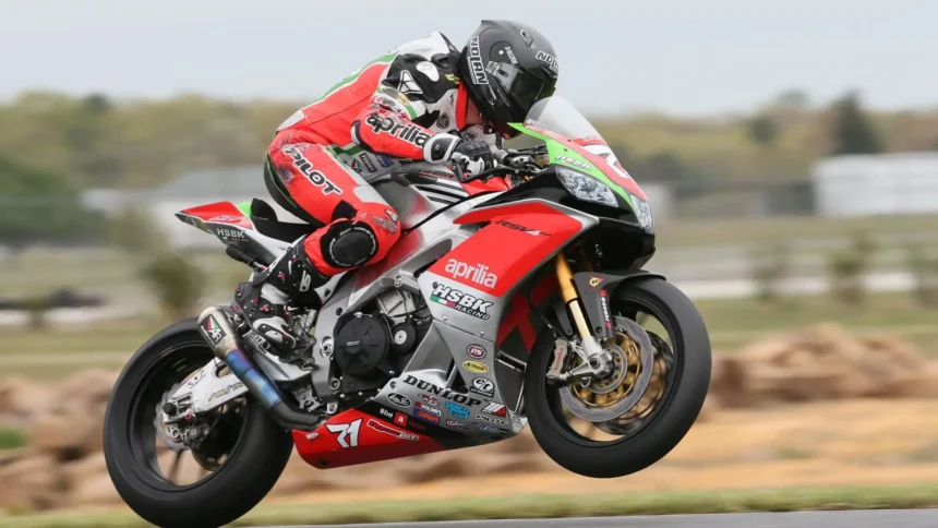 Aprilia RSV4 superbike performing a wheelie during a high-speed race on a racetrack UHD wallpaper