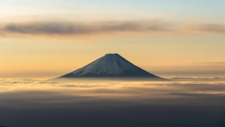 Mount Fuji rising above a sea of clouds beneath a warm golden sunrise sky in Japan wallpaper.