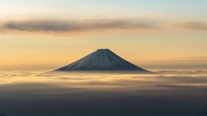 Mount Fuji rising above a sea of clouds beneath a warm golden sunrise sky in Japan wallpaper.