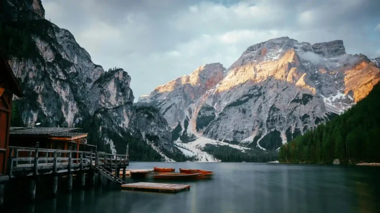 Pragser Wildsee Italy mountain lake with rocky alpine peaks, wooden boats and warm sunlight wallpaper.