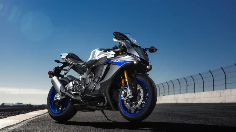 Yamaha YZF R1M carbon fiber superbike with blue wheels parked on a racetrack under a clear blue sky wallpaper.