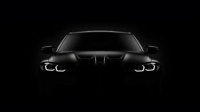 BMW M3 Competition Black Edition viewed from the front, featuring a matte black exterior, illuminated white LED headlights, sculpted hood, and dark kidney grille against a pure black background wallpaper.