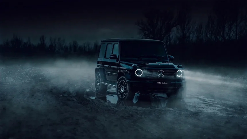 Black Mercedes AMG G63 G-Wagon with glowing circular LED headlights parked on a muddy road surrounded by thick mist, dark trees, and reflections at night wallpaper.