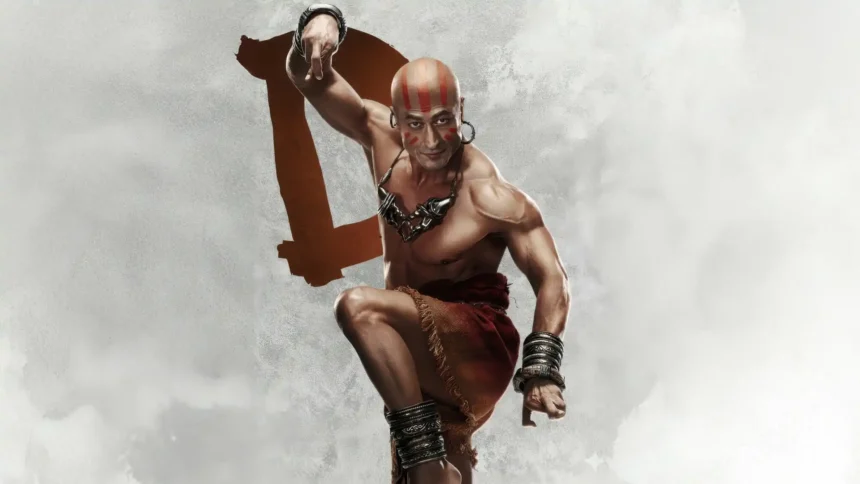 Vidyut Jammwal as Dhalsim in Street Fighter, striking a powerful martial arts pose with red facial markings, metallic accessories, and a smoky white background wallpaper.